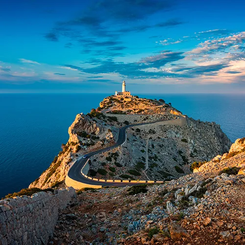 Camino a un faro en un acantilado con el mar y cielo al atardecer.
