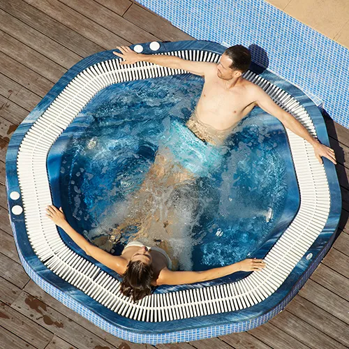 Dos personas relaj&aacute;ndose en un jacuzzi al aire libre.