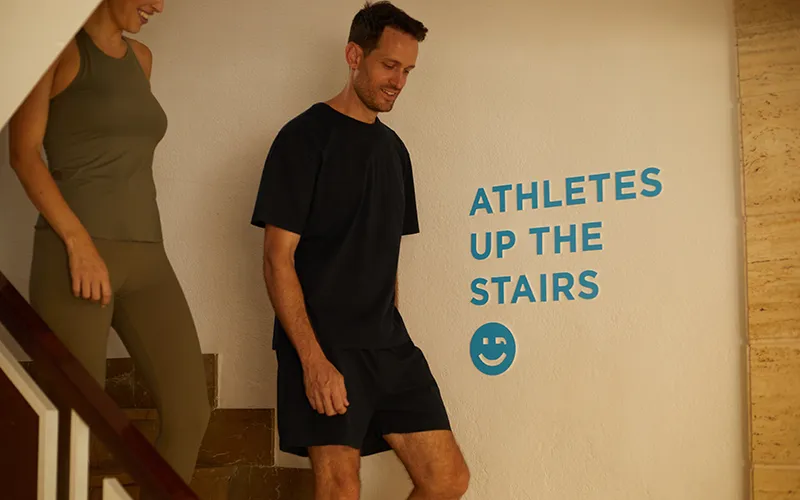 Personas bajando las escaleras junto a un letrero que dice "ATHLETES UP THE STAIRS".