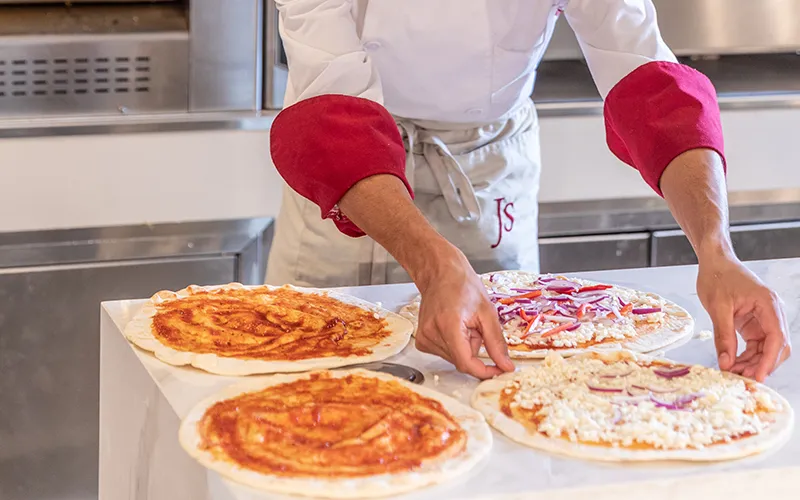 Chef preparando pizzas con diferentes ingredientes en una cocina.