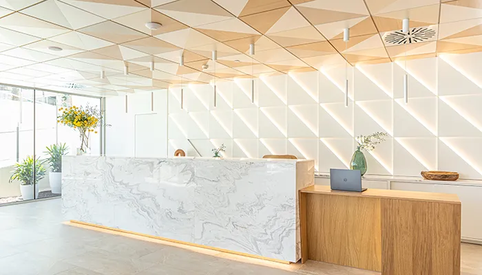 Recepci&oacute;n moderna con mostradores de m&aacute;rmol y madera, y paredes geom&eacute;tricas.