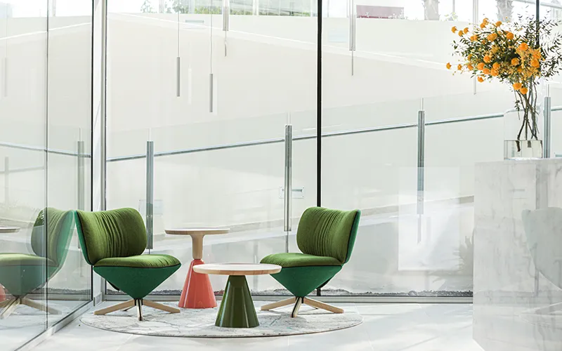 Sala moderna con sillas verdes, mesas peque&ntilde;as y flores naranjas.