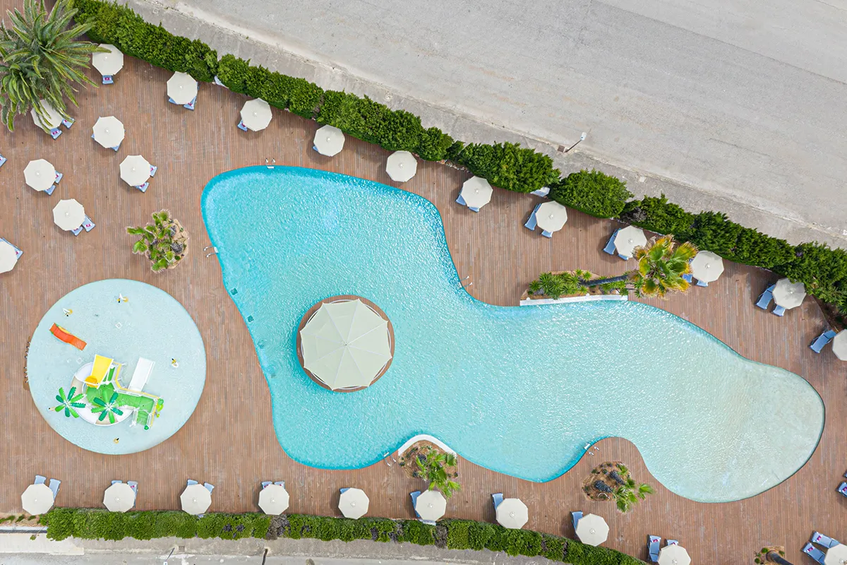 Vista a&eacute;rea de una piscina con sombrillas y un &aacute;rea de juegos acu&aacute;ticos.