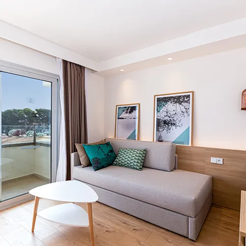 Sala moderna con sof&aacute; gris, mesa blanca y cuadros decorativos. Ventana a la izquierda.