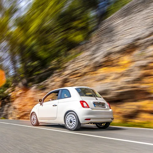 Auto blanco peque&ntilde;o circulando r&aacute;pido por una carretera junto a un muro.
