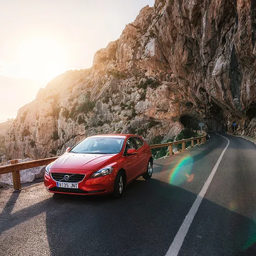 Coche rojo en carretera monta&ntilde;osa al atardecer.