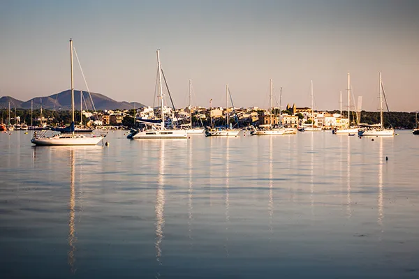 Veleros flotando en un puerto tranquilo al atardecer, con monta&ntilde;as al fondo.