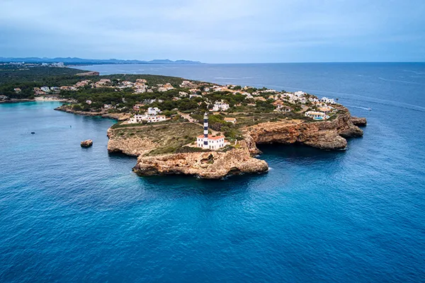 Vista a&eacute;rea de un faro en una costa rocosa rodeada de mar azul.