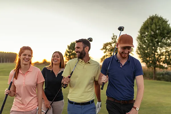 Cuatro personas caminando felices en un campo de golf al atardecer.