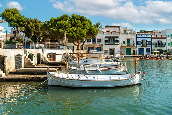 Barcos blancos atracados en un puerto con casas al fondo y cielo despejado.