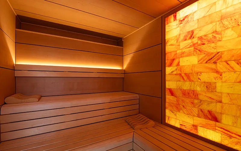Sauna de madera iluminada con pared de piedra naranja.