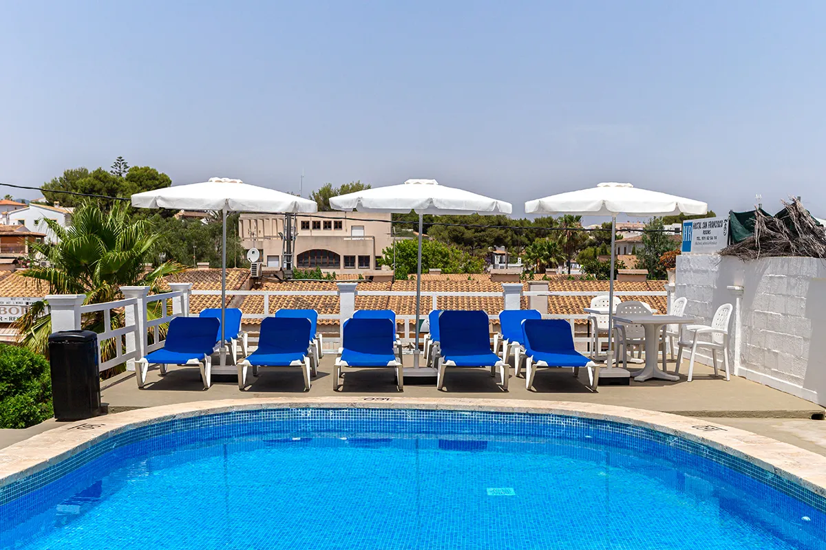 Piscina con tumbonas azules y sombrillas blancas bajo un cielo despejado.
