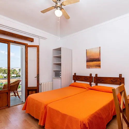 Habitaci&oacute;n luminosa con dos camas, ventilador y balc&oacute;n con vista.