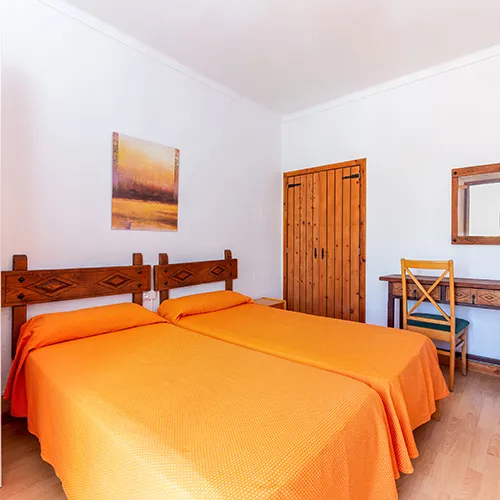 Habitaci&oacute;n doble con camas naranjas, escritorio y armario de madera.