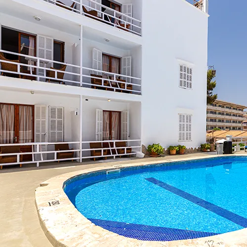 Edificio blanco con balcones junto a una piscina azul al aire libre.