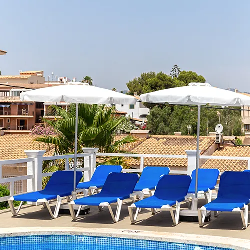 Sillas azules y sombrillas blancas junto a una piscina en una terraza soleada.