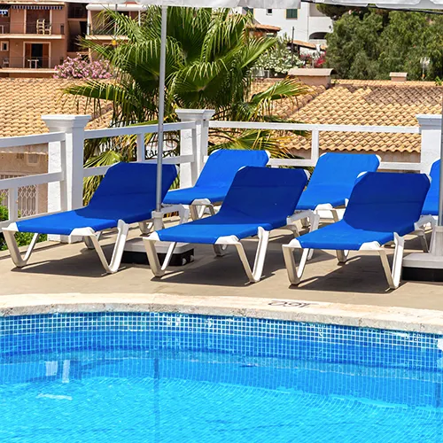 Camastros azules junto a una piscina con mosaico y barandales blancos.