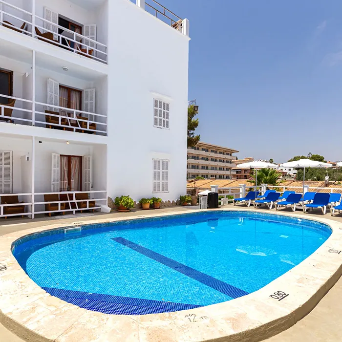 Edificio blanco junto a una piscina con tumbonas azules bajo el cielo despejado.