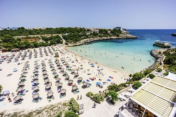 Playa con sombrillas y ba&ntilde;istas en el agua, rodeada de vegetaci&oacute;n.