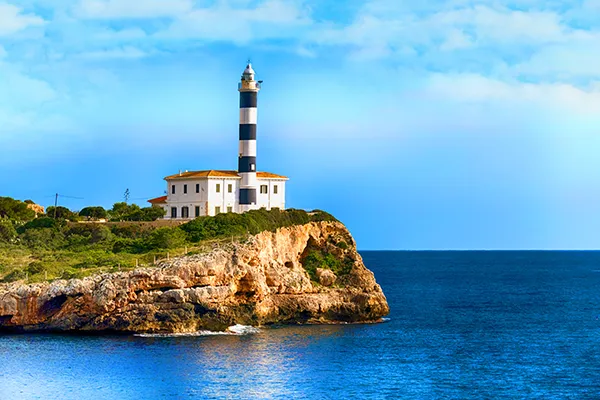 Faro blanco y negro sobre un acantilado junto al mar bajo un cielo azul.