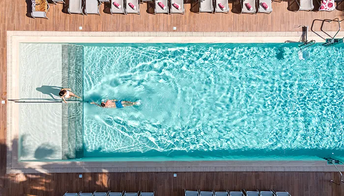 Vista a&eacute;rea de una piscina con dos personas nadando y tumbonas alrededor.