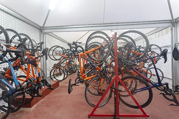 Bicicletas anaranjadas y azules colgadas en racks en una habitaci&oacute;n techada.