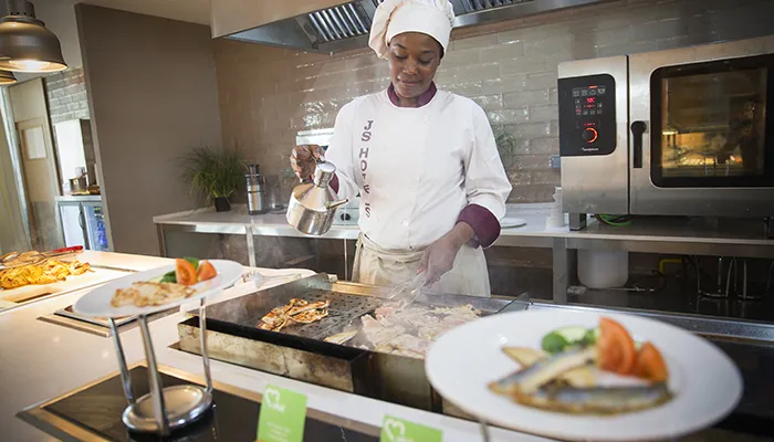 Chef cocinando frente a una parrilla en una cocina profesional.