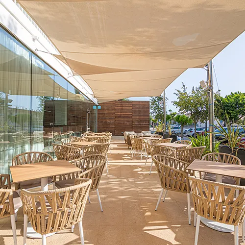 Terraza de caf&eacute; con sillas y mesas al aire libre bajo un toldo.
