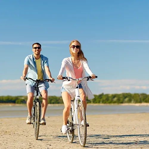 Personas montando bicicletas en la playa bajo un cielo despejado.