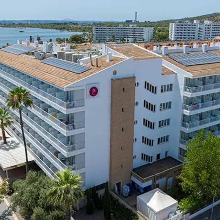 Edificio blanco con balcones, cerca de un lago y rodeado de &aacute;rboles.