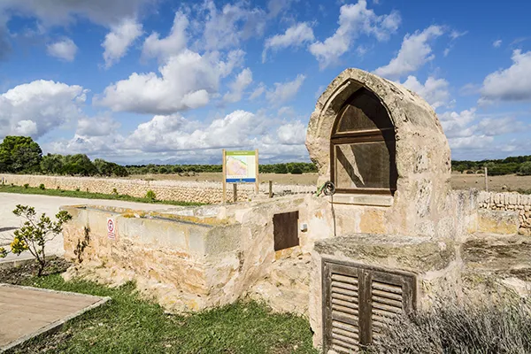 Paisaje rural con antiguo pozo de piedra y cielo azul con nubes.