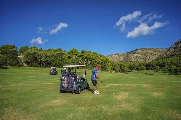 Persona juega golf en un campo verde con cielo azul y carrito de golf.