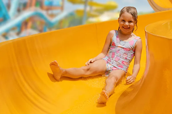 Ni&ntilde;a sonriendo en un tobog&aacute;n amarillo acu&aacute;tico.