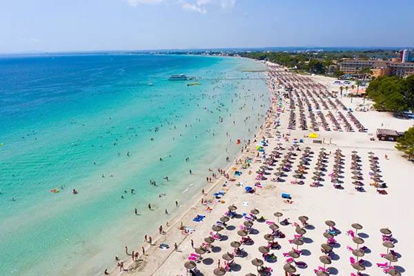 Playa concurrida con sombrillas y ba&ntilde;istas en la costa de aguas turquesas.
