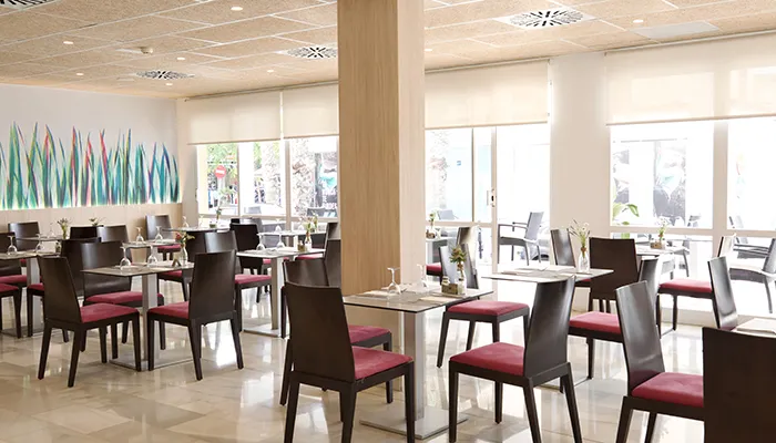 Restaurante moderno con sillas rojas, mesas arregladas y decoraci&oacute;n colorida en pared.