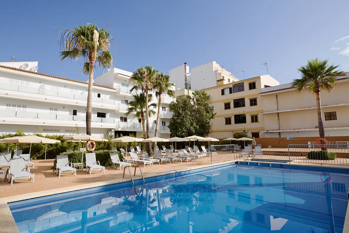Piscina con tumbonas y sombrillas en hotel, rodeada de palmeras y edificios.