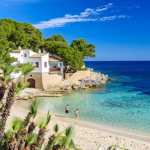Casa junto al mar con playa, palmeras y agua cristalina bajo un cielo azul.