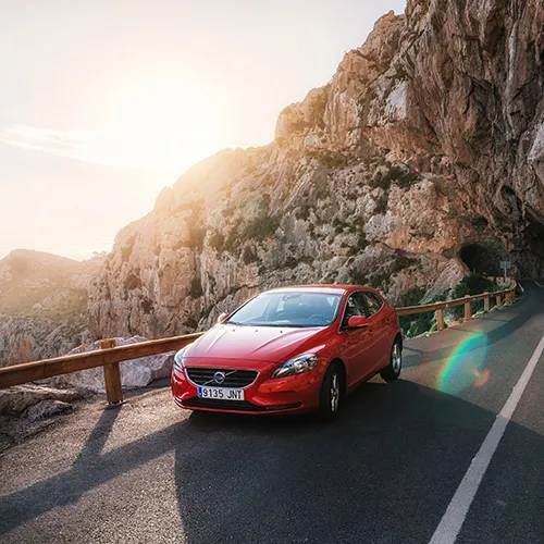 Auto rojo en una carretera de monta&ntilde;a al atardecer.