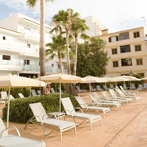 Sillas de playa vac&iacute;as con sombrillas y palmeras en un hotel.