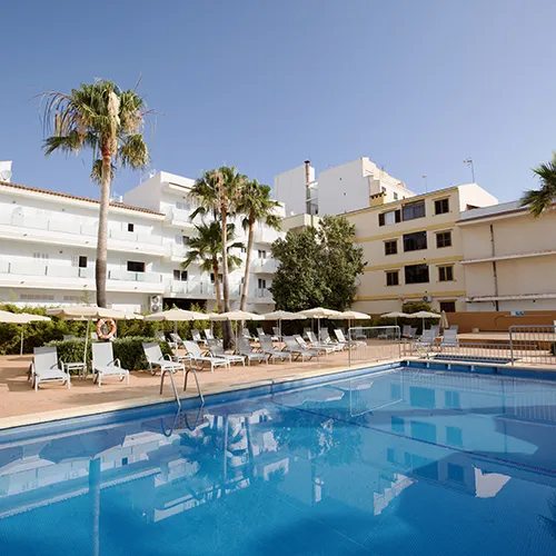 Piscina al aire libre con tumbonas y palmeras bajo un cielo despejado.