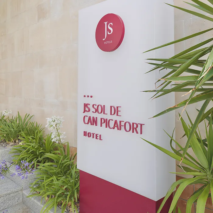 Letrero del hotel JS Sol de Can Picafort rodeado de plantas verdes.