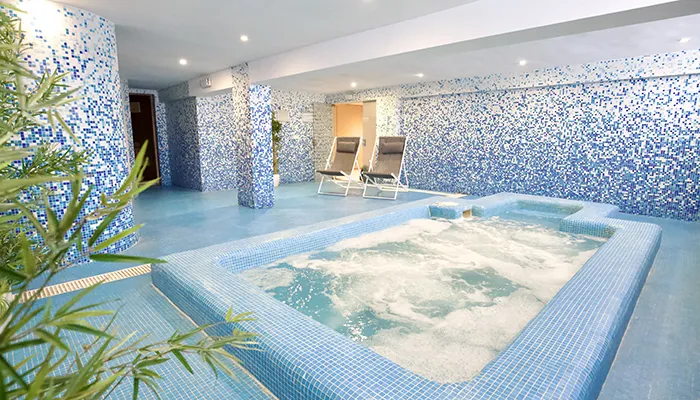 Piscina de hidromasaje en interior decorado con azulejos azules y tumbonas.