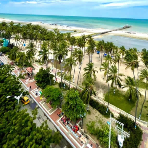 Vista aérea de una ciudad costera con playa y muelle bajo un cielo despejado.