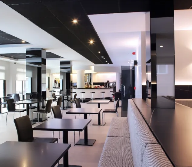Un restaurante moderno con mesas negras, sillas y barra de bar al fondo.