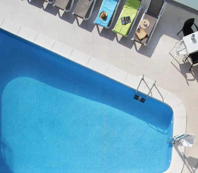 Vista aérea de una piscina con tumbonas y una mesa con sillas en el área circundante.