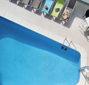 Piscina vista desde arriba con tumbonas y sillas alrededor en un área soleada.
