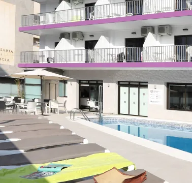 Piscina al aire libre con tumbonas y edificio de hotel en el fondo.