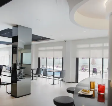 Sala moderna con sillas, mesas y bebidas frente a ventanas amplias y una decoración minimalista.