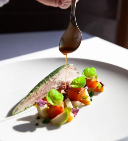 Plato gourmet con salsa, verduras y carne elegante en presentaci&oacute;n art&iacute;stica.