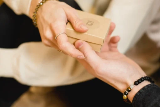 Personas intercambiando una peque&ntilde;a caja de regalo marr&oacute;n entre sus manos.